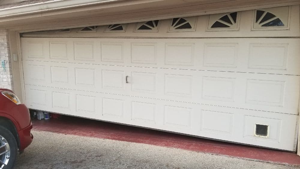White garage door with decorative windows, parked red car in foreground.