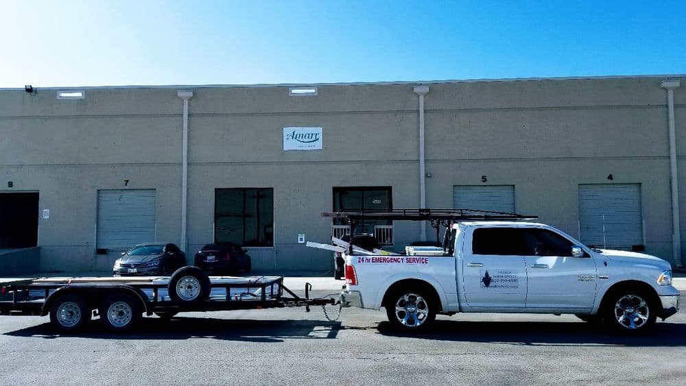White pickup truck towing a trailer parked outside a warehouse with loading docks.