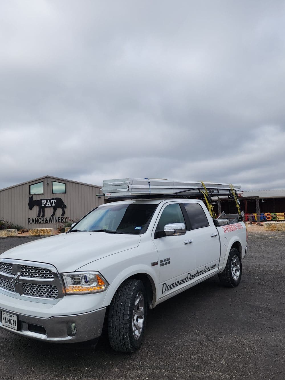 White pickup truck with ladder parked near Fat Ranch & Winery, showcasing Dominant Doors branding.