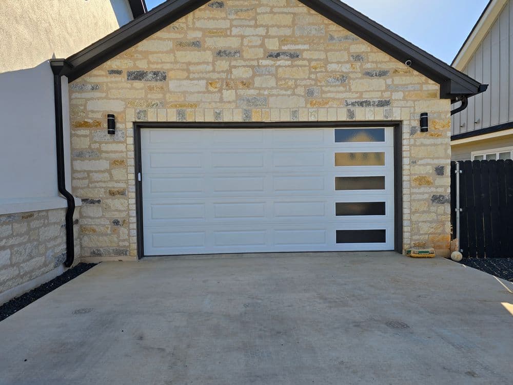 Modern garage door on a stone house exterior with sleek design and large windows.
