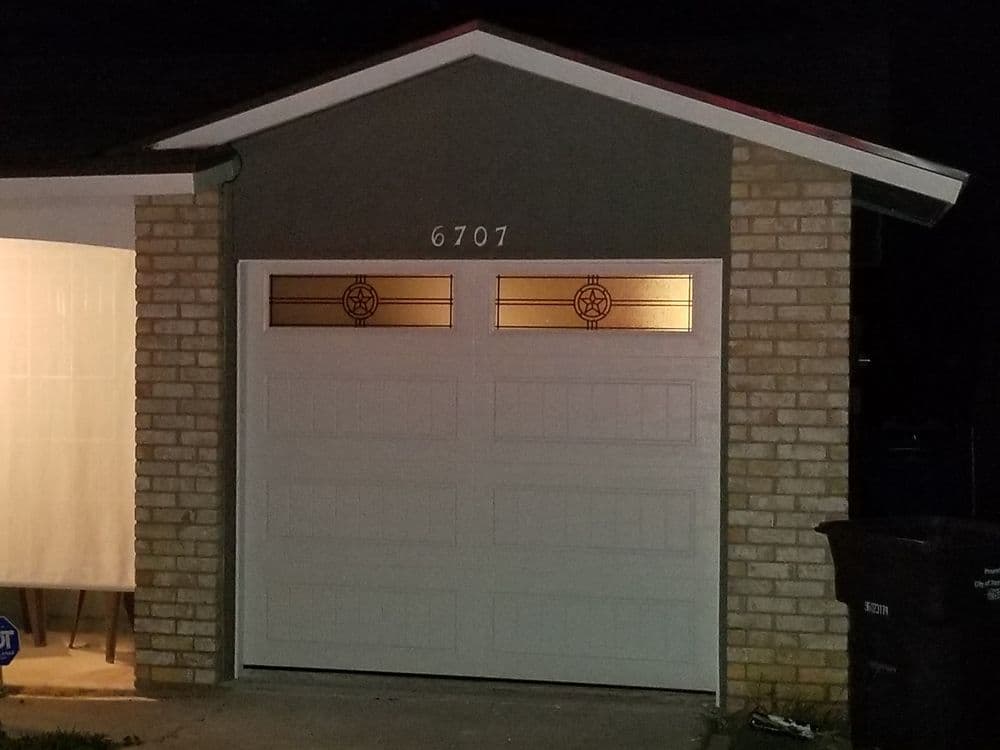 Garage door with decorative glass panels, house number 6707, nighttime setting.