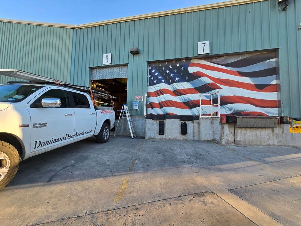 White pickup truck parked outside a warehouse with a large American flag mural on the wall.