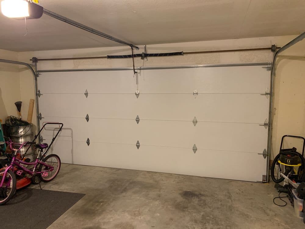 White garage door with decorative hardware, bicycles, and tools in a well-lit garage.
