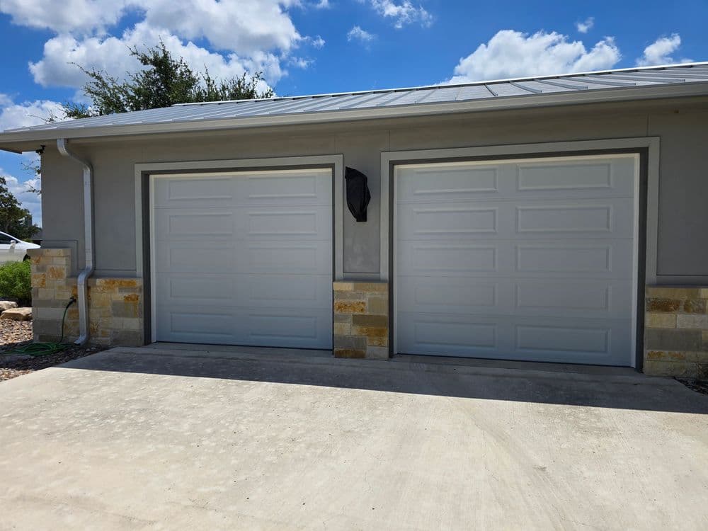 Modern two-car garage with gray doors and stone accents under a blue sky.