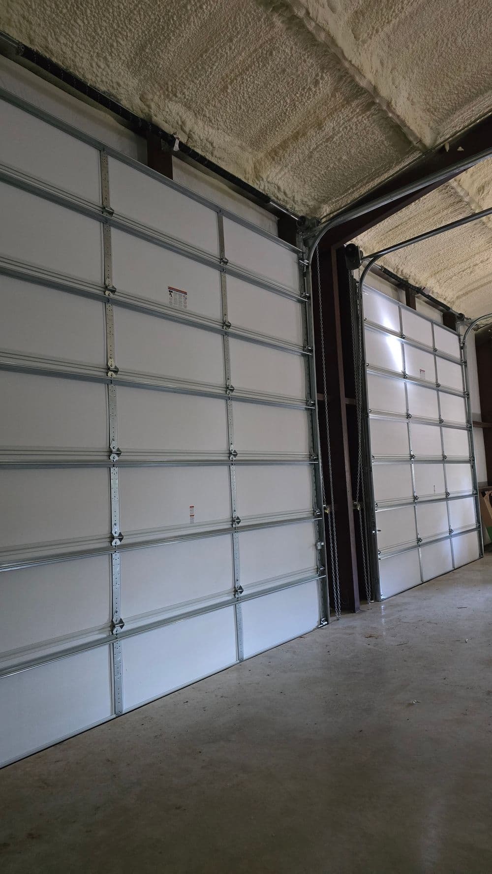 Two large, white garage doors in a spacious indoor garage setting.