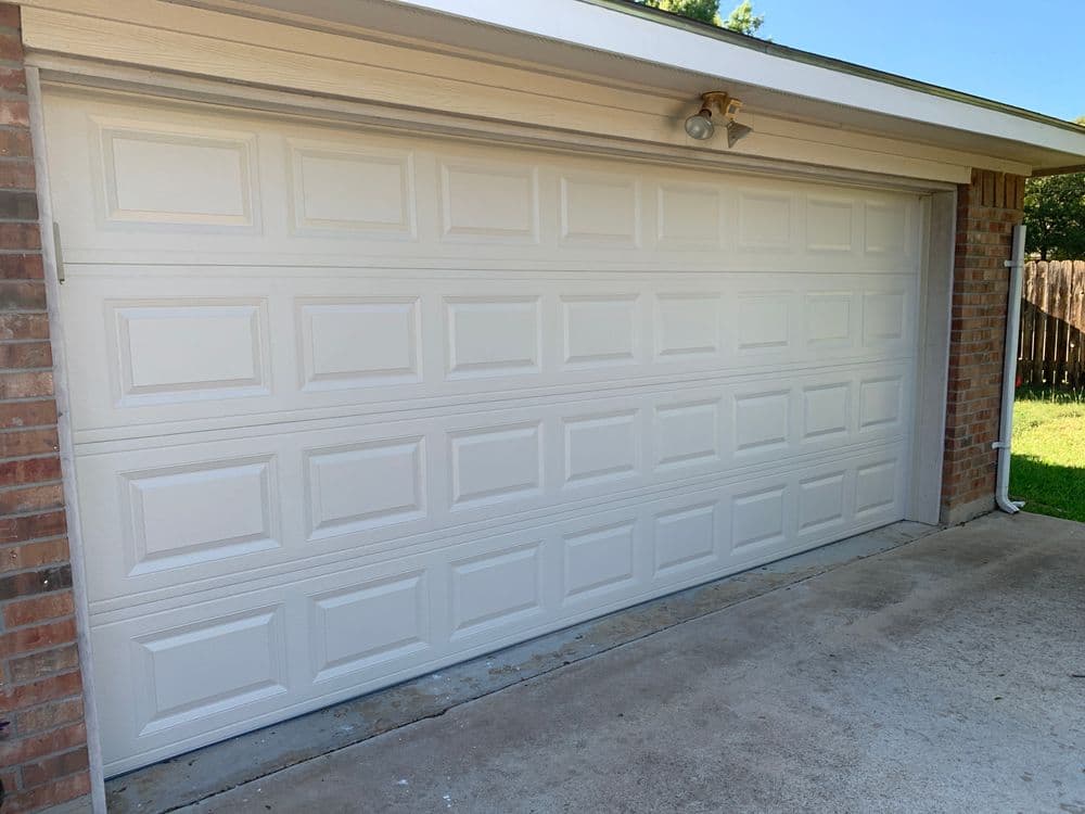 White garage door with a brick exterior and well-maintained concrete driveway.