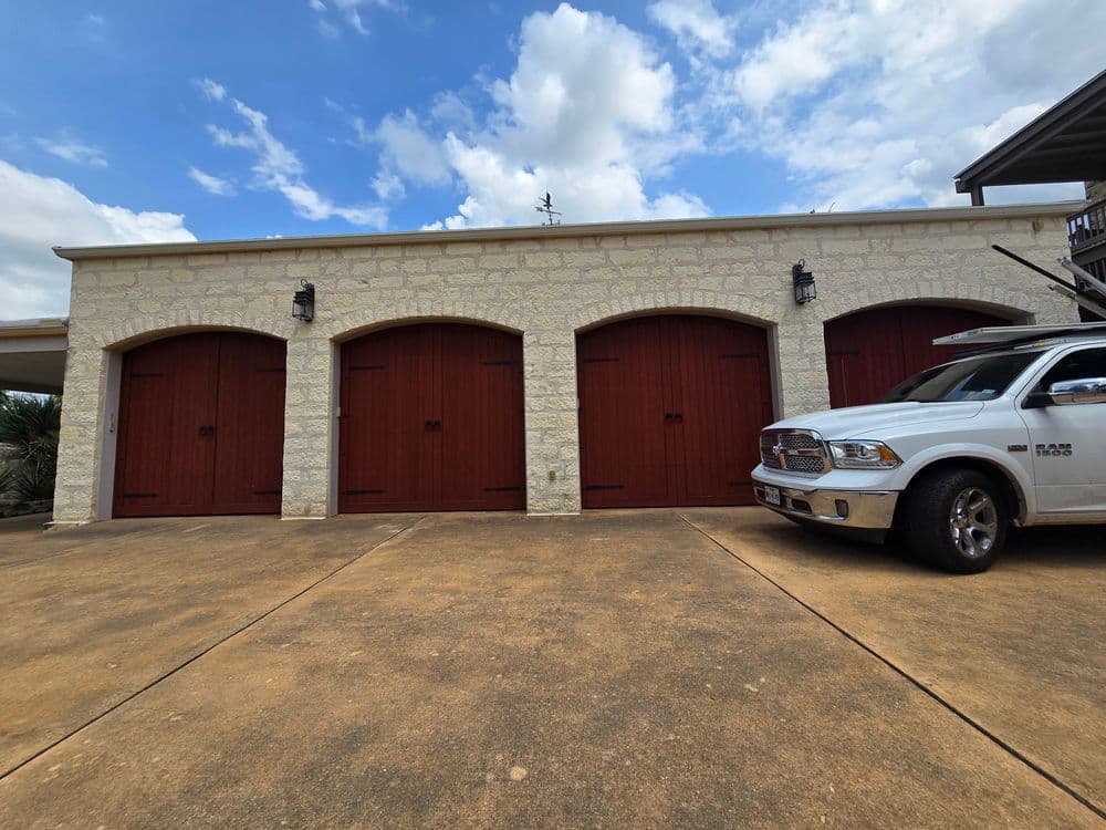 Stone garage with red doors and a silver truck parked in front under a blue sky.