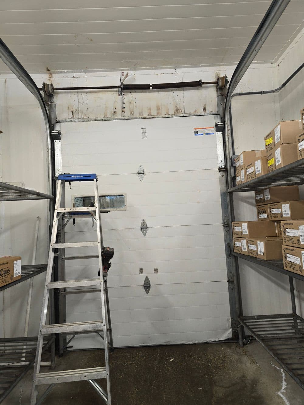 Interior of a garage with a white door, ladder, and shelves filled with boxes.