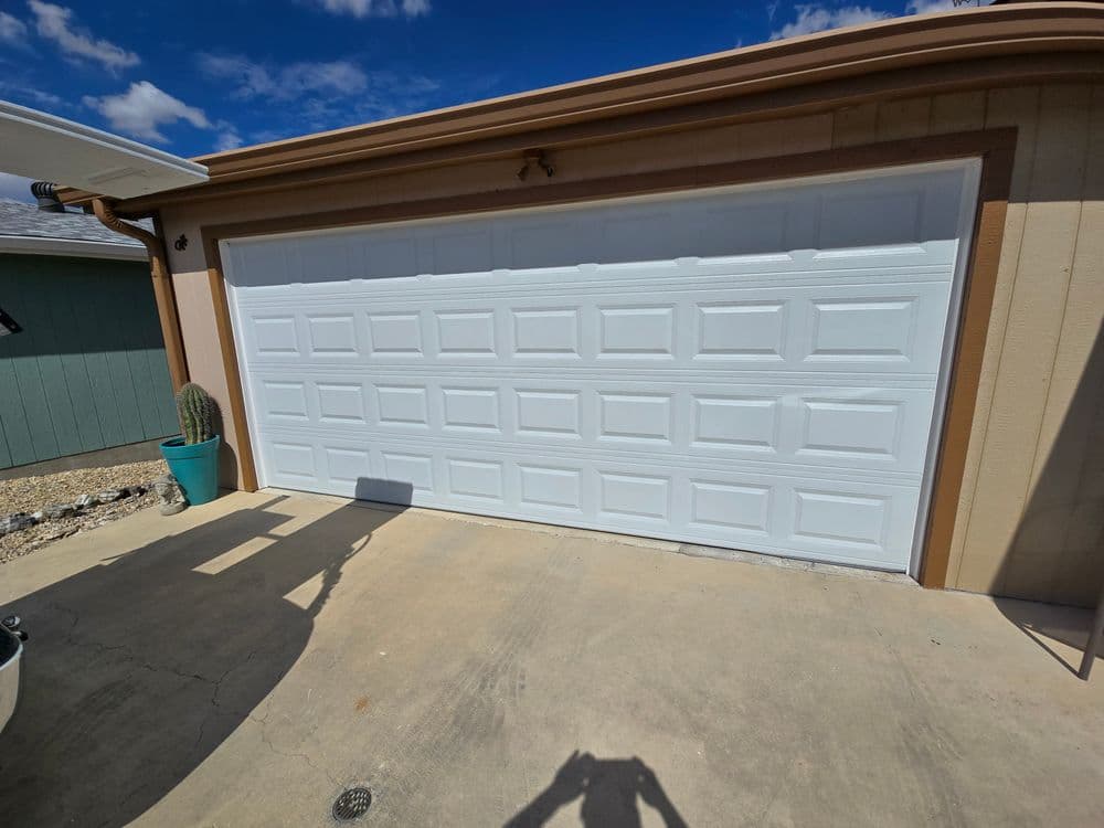 White garage door with decorative paneling, outdoor setting, blue sky and cactus nearby.