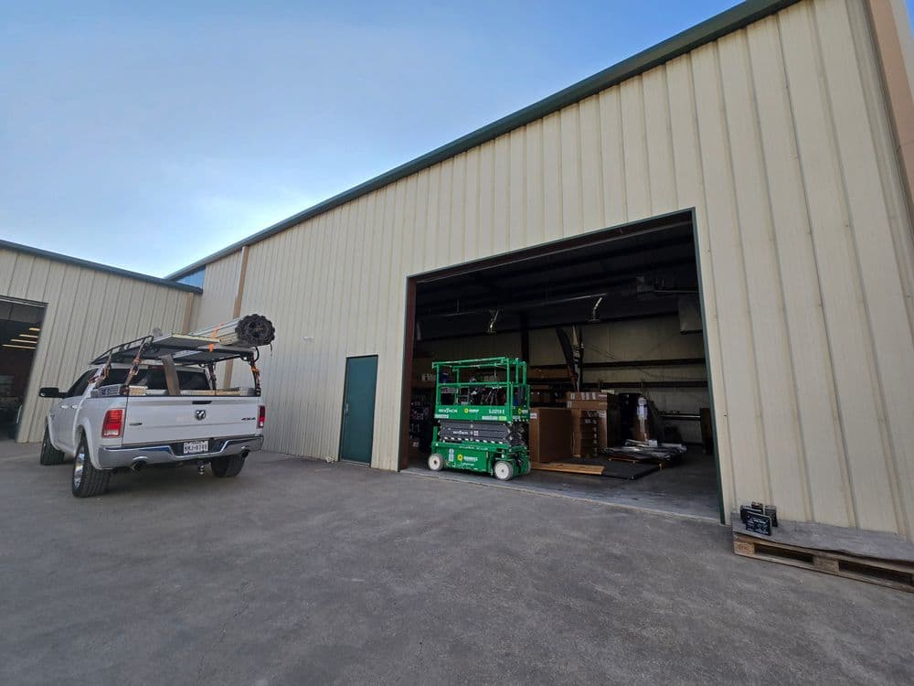 Warehouse exterior with a pickup truck and a green lift, showcasing loading area and equipment.