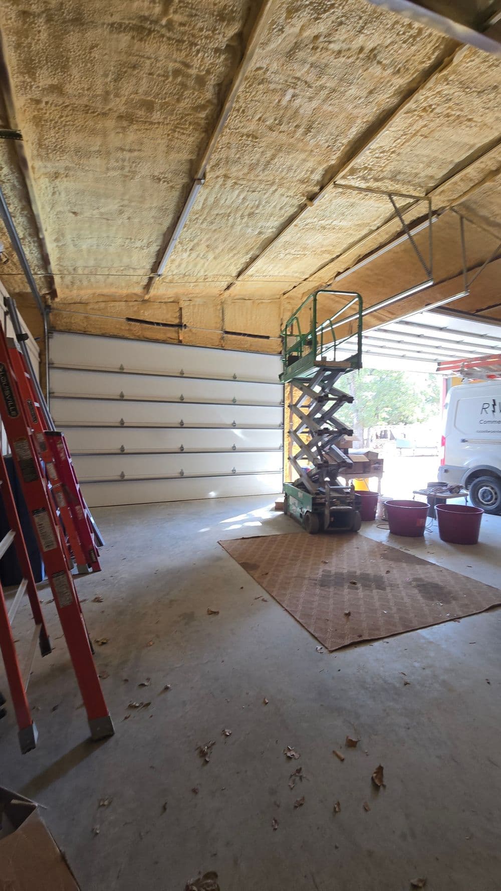Empty garage interior with insulation, ladders, and a scissor lift ready for use.