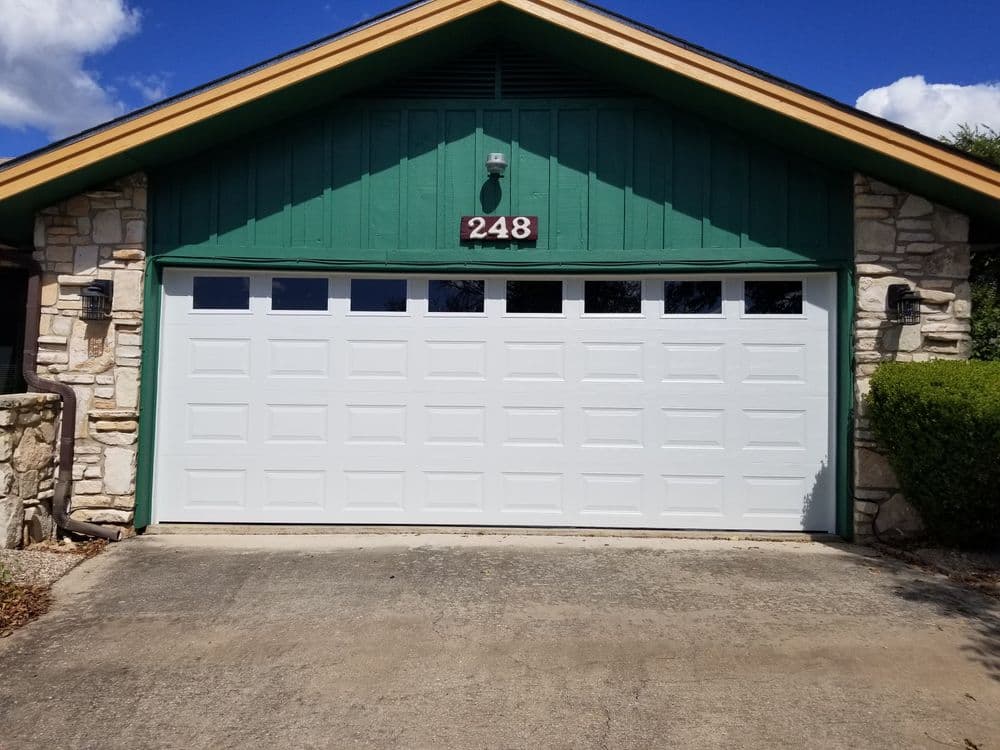 White garage door on a stone house with green accents, featuring windows and house number 248.