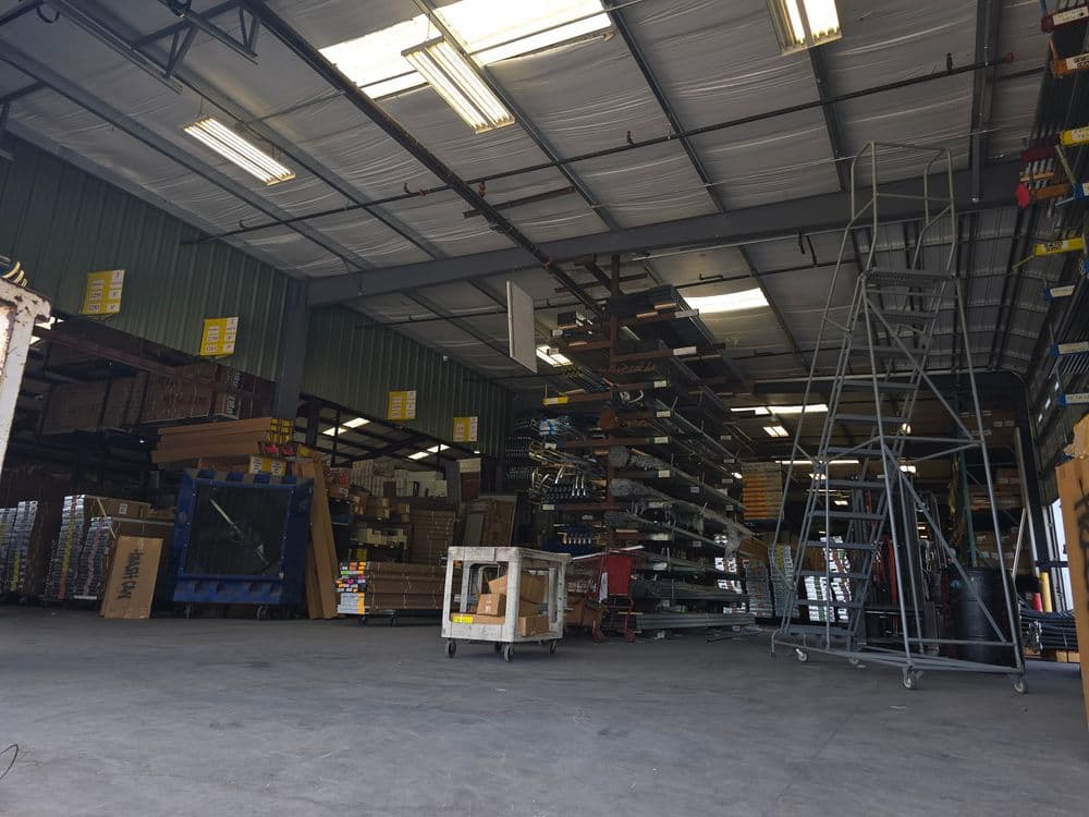 Interior of a warehouse showing shelves filled with supplies and equipment, lit by overhead lights.