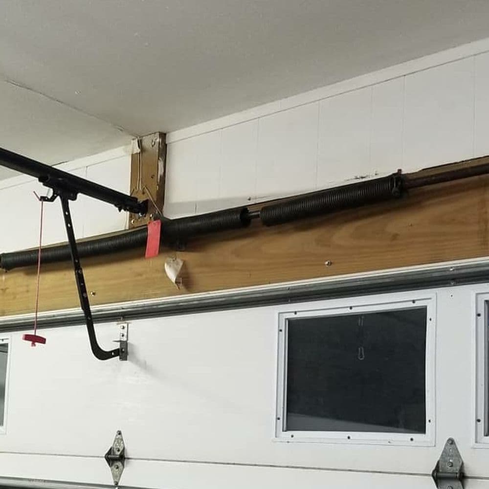 Garage door spring mechanism with pulley, wall-mounted, showing structural support elements.