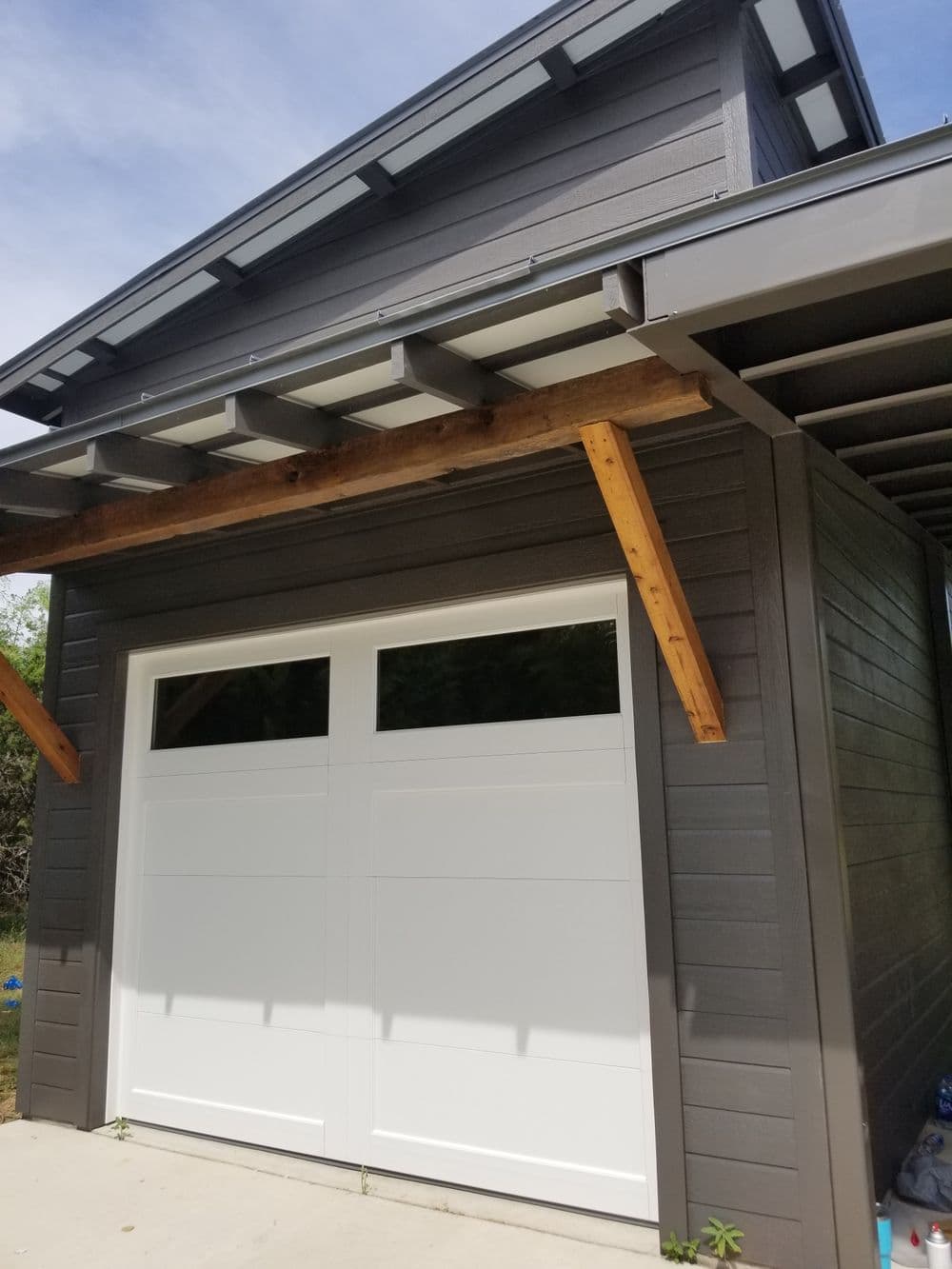 Modern garage with white doors, wooden accents, and sleek gray exterior. Bright sky above.