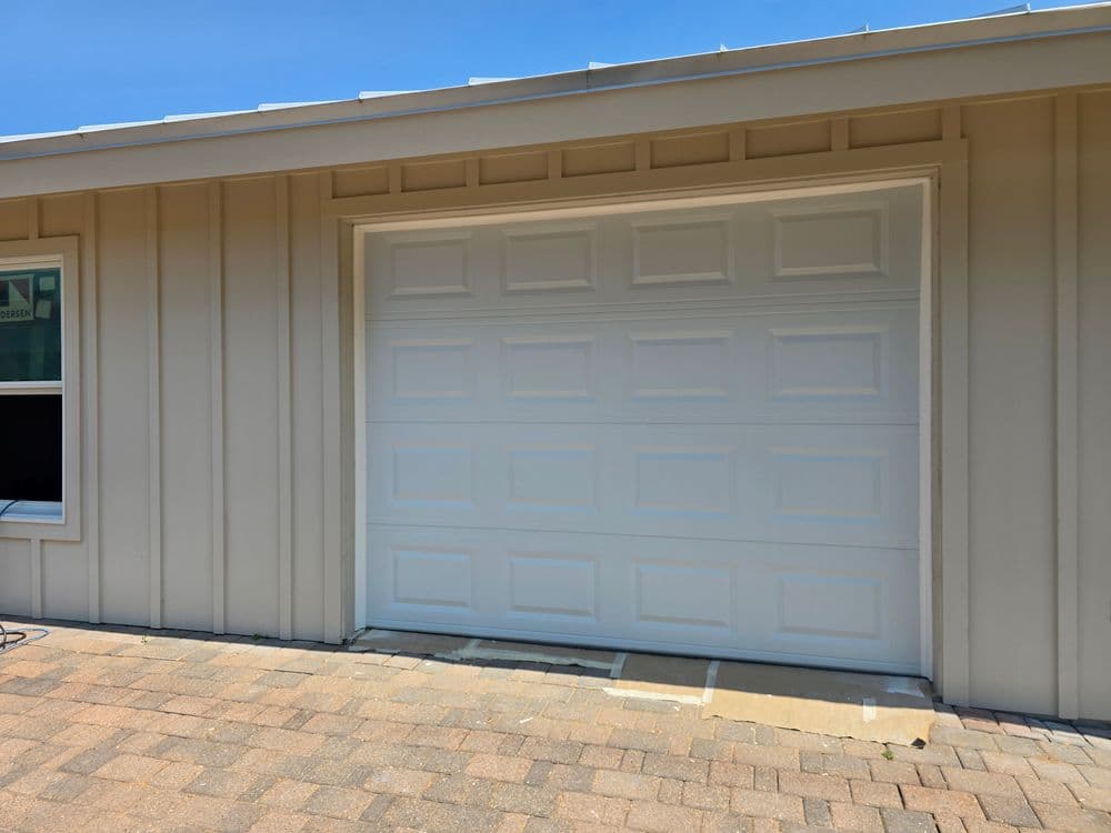White garage door on a beige house exterior with a paved driveway under a clear blue sky.