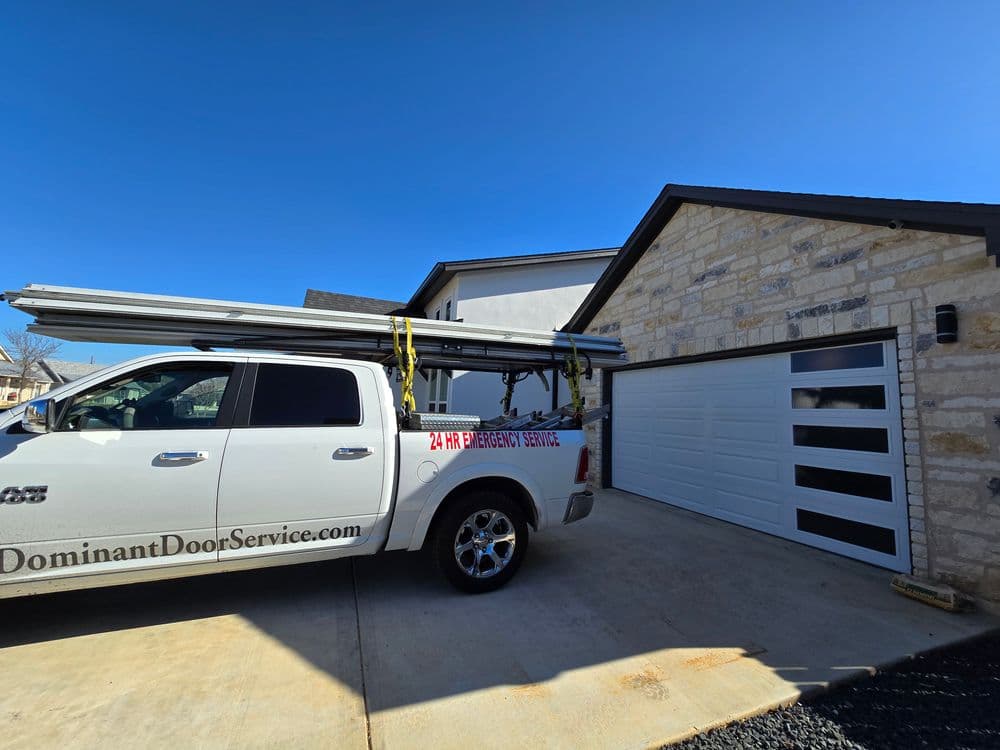 Dominant Door Service truck parked outside a modern home with a garage door and tools.