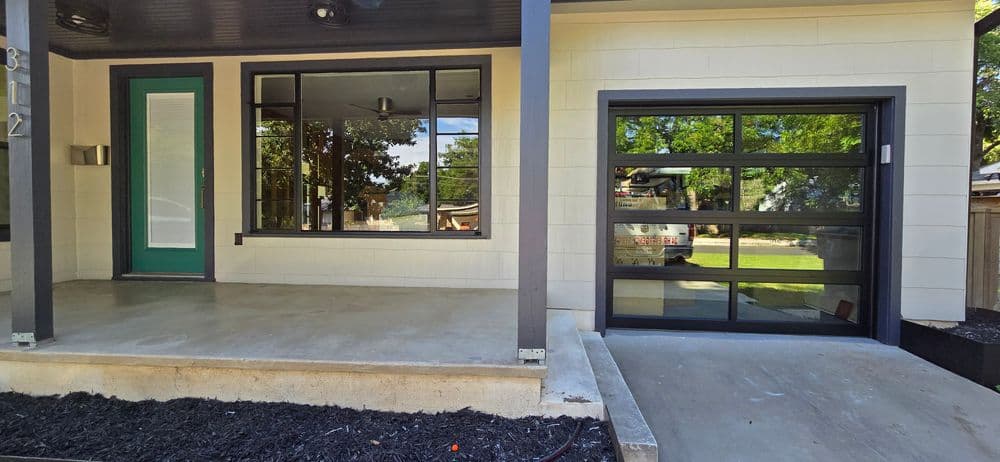 Modern home exterior featuring large windows, a sleek garage door, and a landscaped entryway.