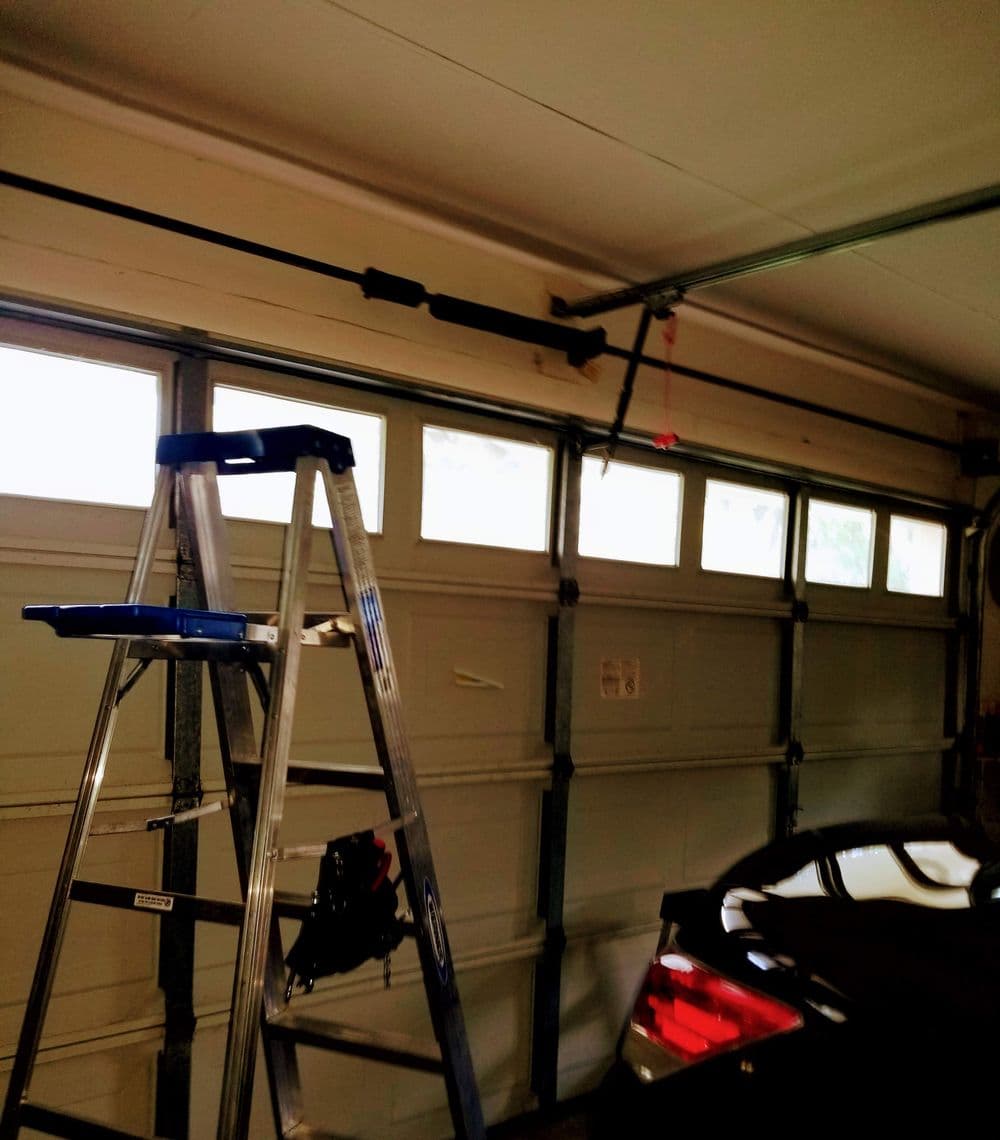 Ladder in a garage next to an open garage door and a parked car.