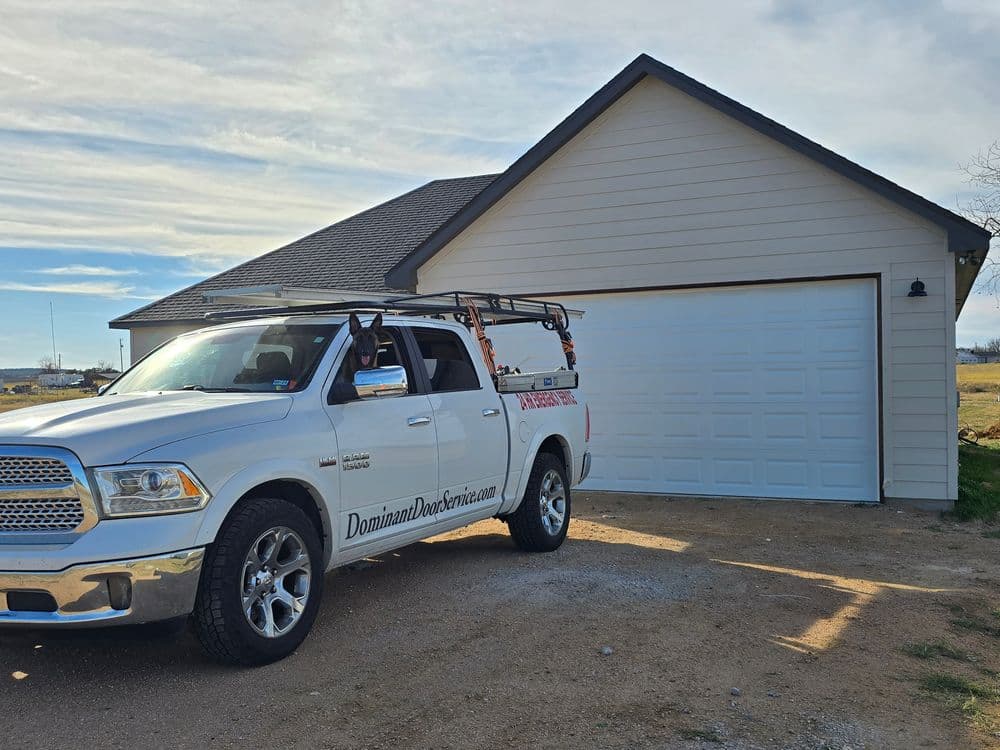 White pickup truck parked in front of a house with a garage, featuring a ladder rack.