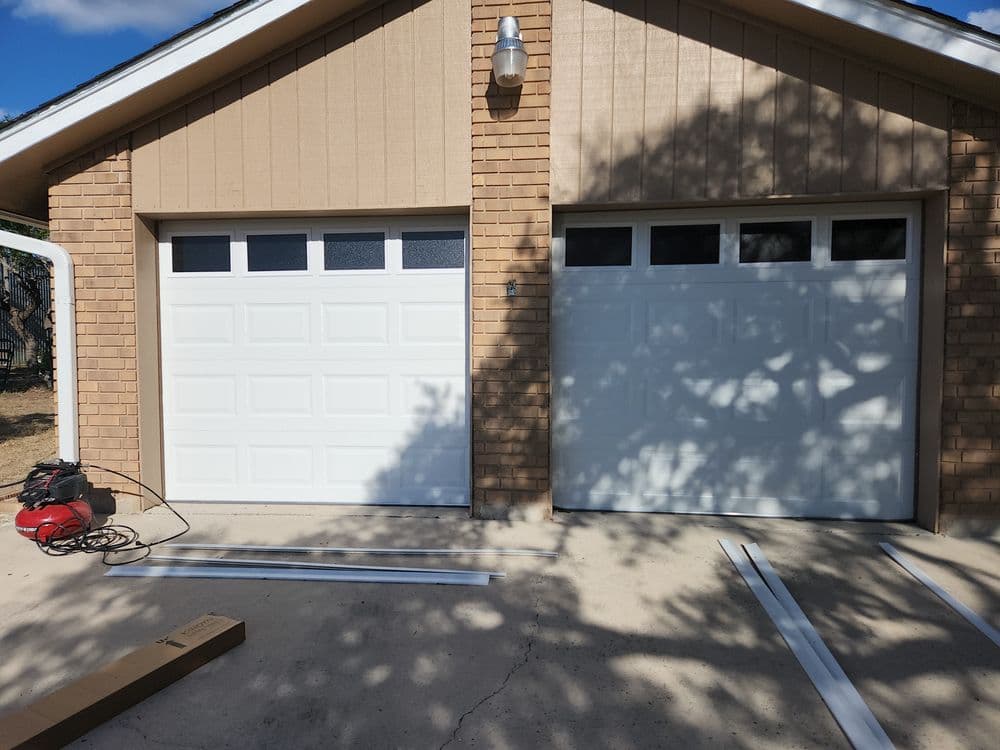 New garage doors installed on a home, with tools and materials nearby.