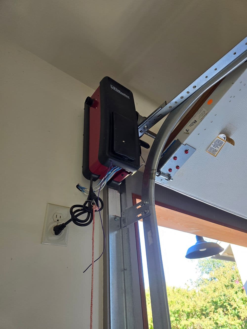 Garage door opener mounted on a wall with power outlet and garage door track visible.