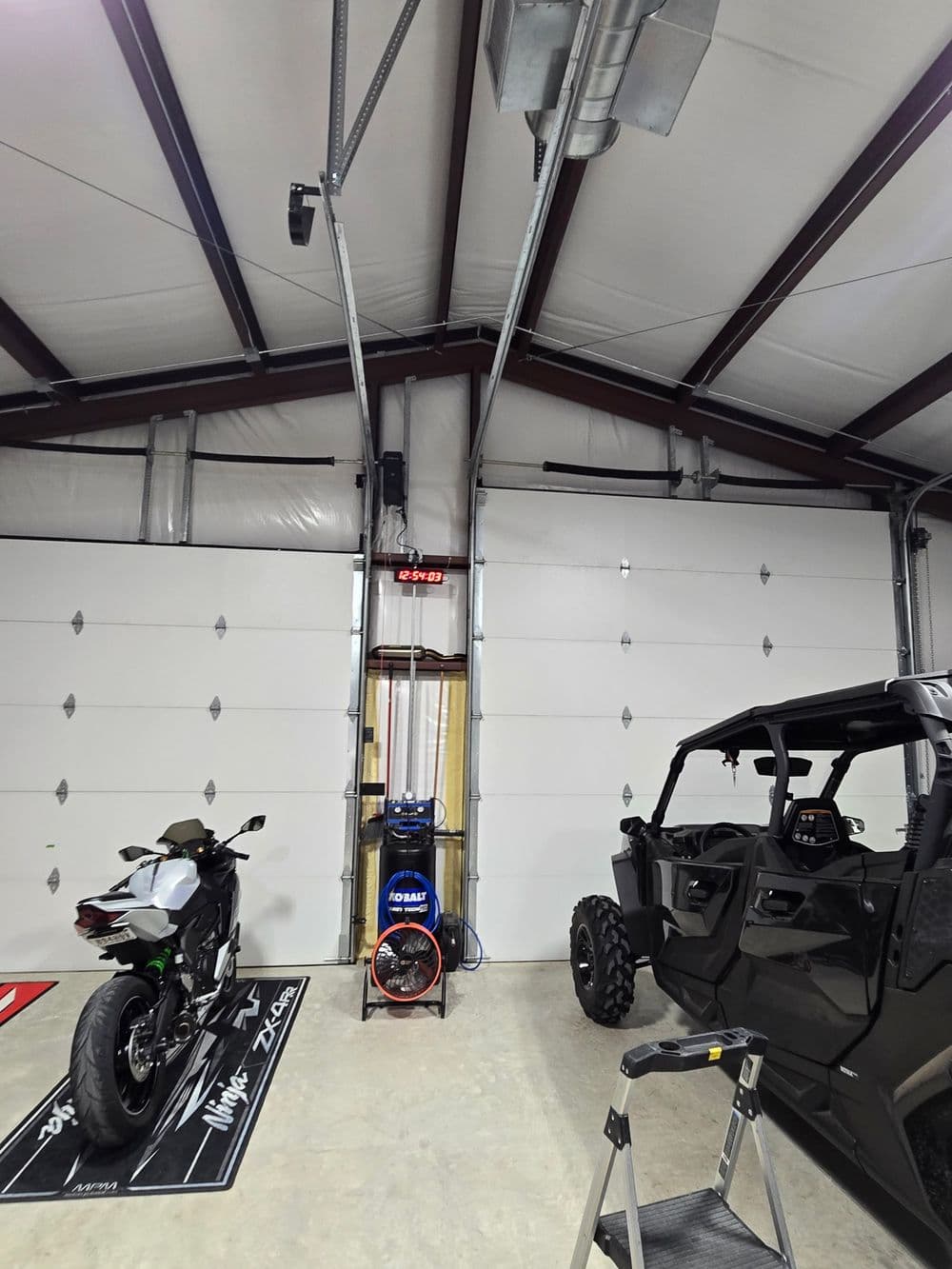 Motorcycle and off-road vehicle in modern garage with industrial-style overhead fans.