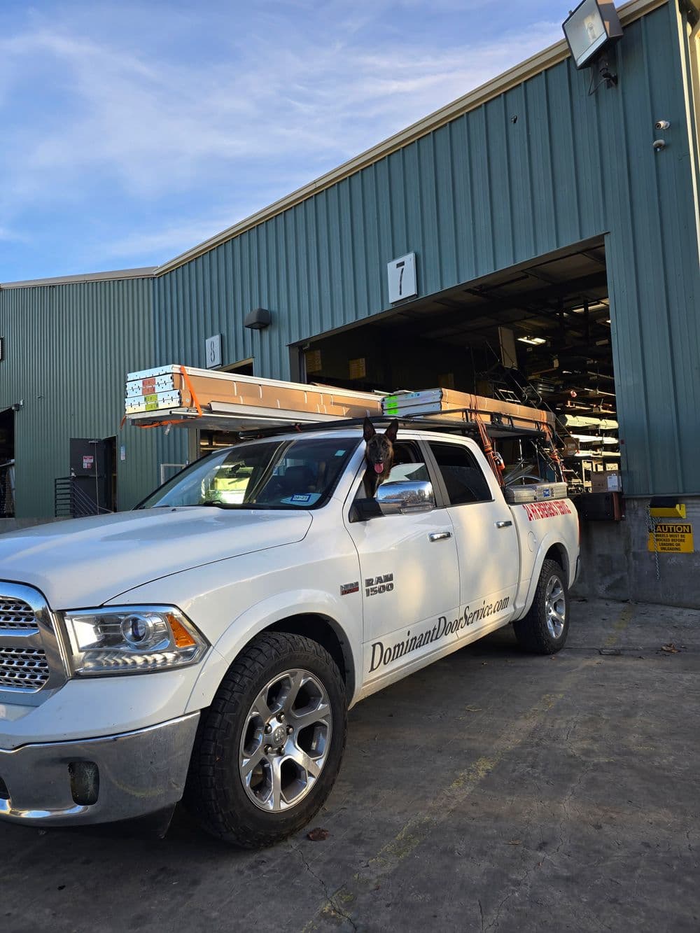 White truck with ladders parked outside a warehouse for Dominant Door Services.