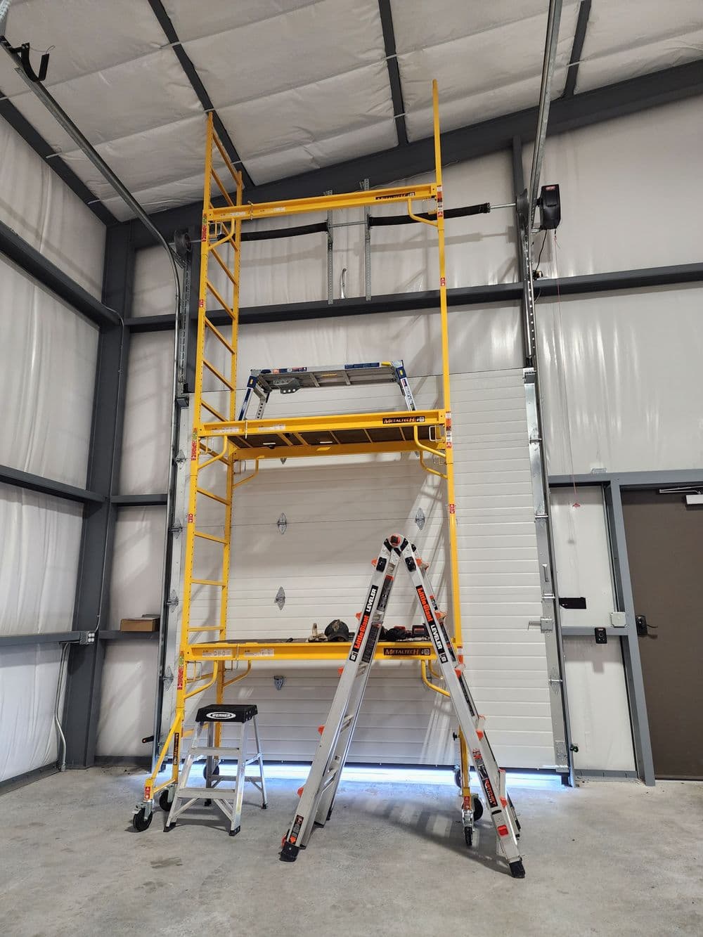 Yellow scaffolding setup in industrial space with a ladder against a wall.