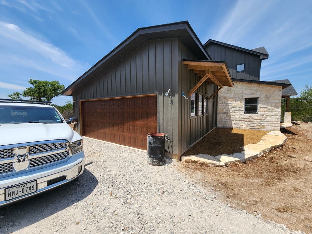 Modern home exterior with wooden garage door and stone accents, surrounded by new landscaping.