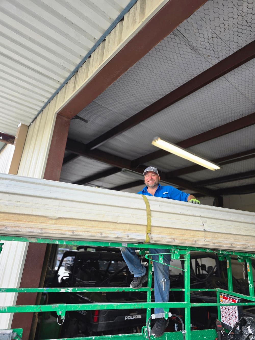 Worker on a scaffold inside a warehouse, handling materials with safety gear.