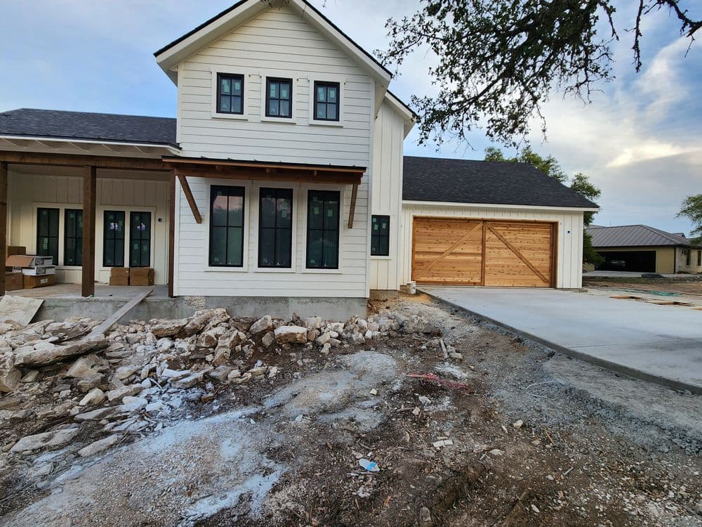 Newly constructed modern farmhouse with wooden garage door and raw landscaping.