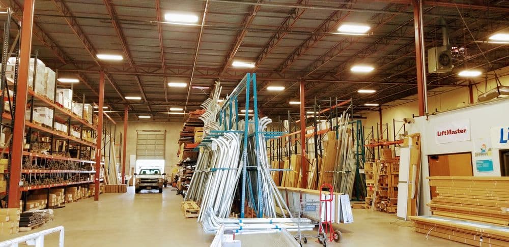 Warehouse interior with shelves of building materials and equipment, bright lighting overhead.