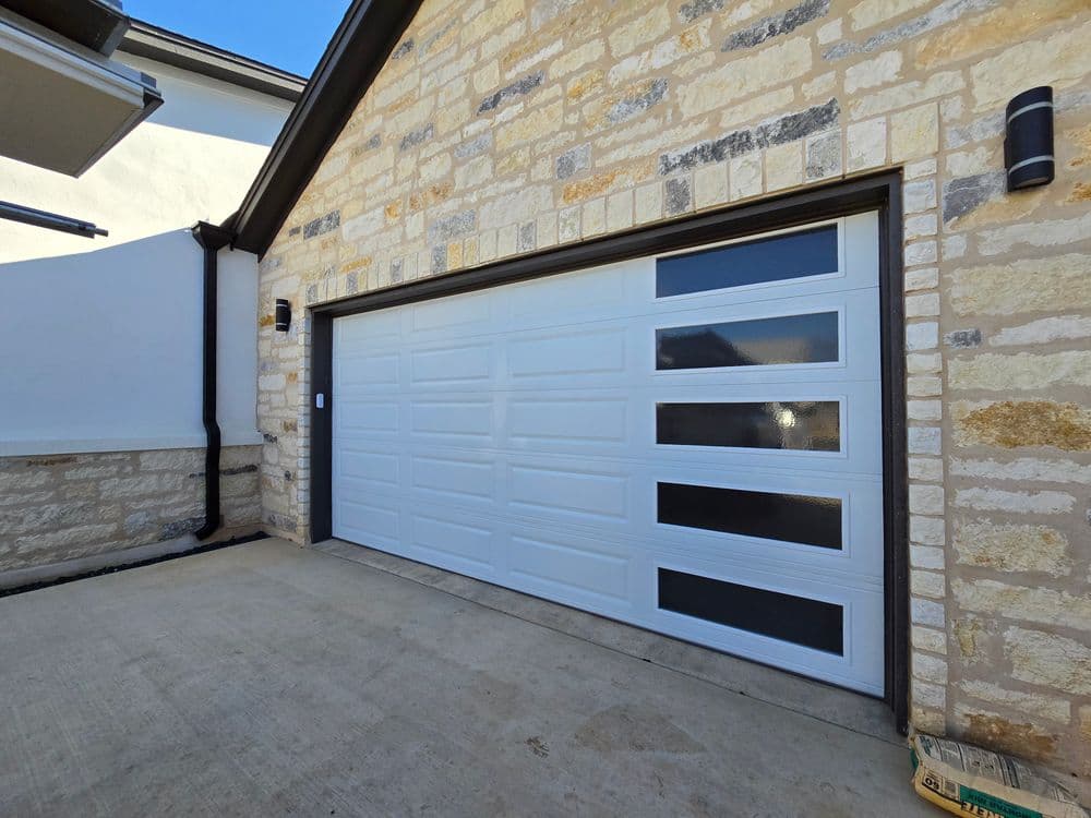 Modern residential garage door with vertical windows and stone wall exterior.