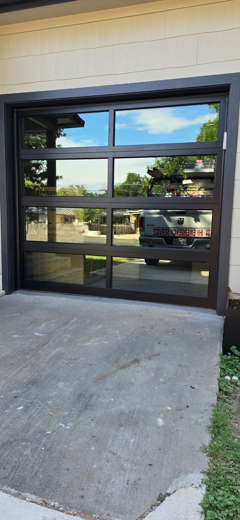 Modern glass garage door with sleek black frame and driveway reflection.