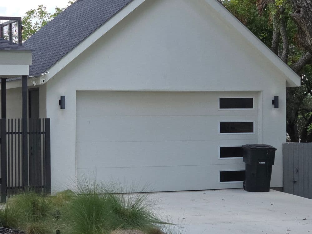 Modern white garage with large windows, sleek design, and green trash can outside.