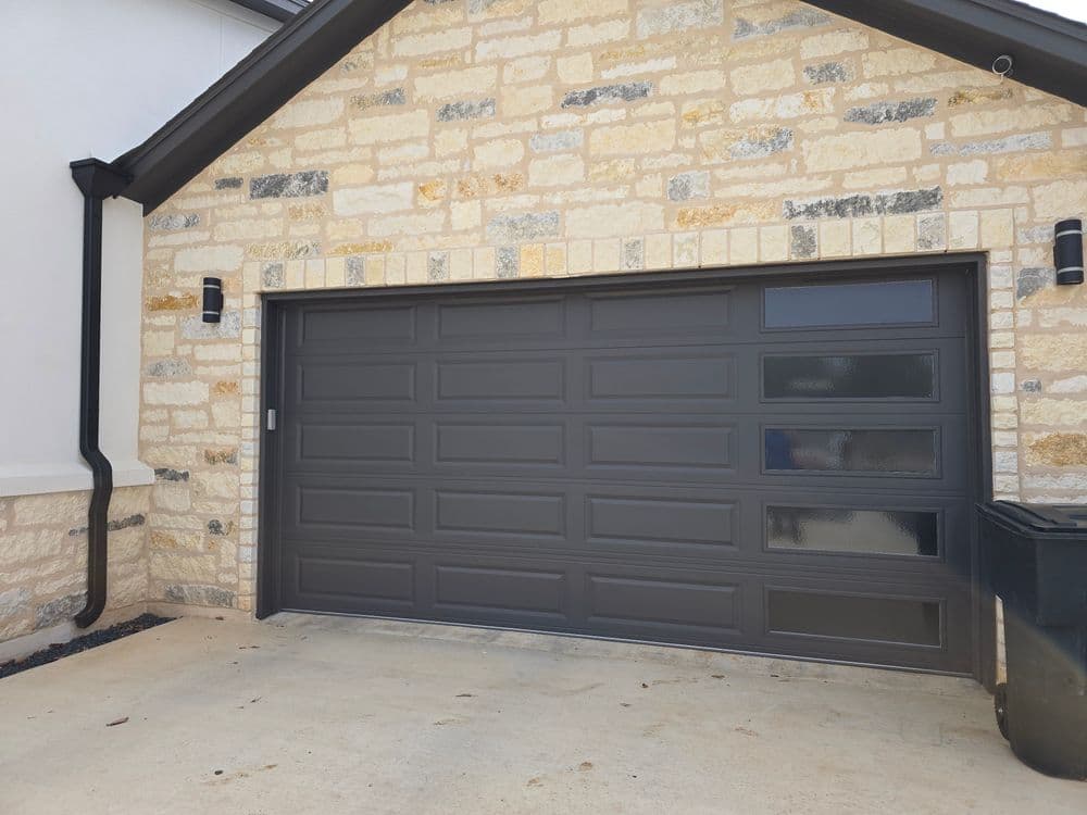 Modern garage door with horizontal panels, stone wall exterior, and clear window accents.