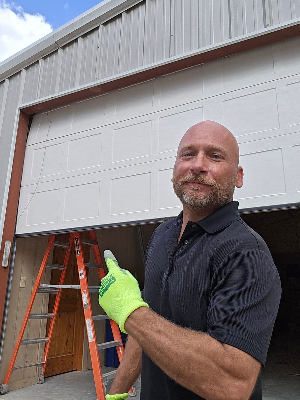 Man in safety gloves pointing at a garage door under construction with a ladder nearby.