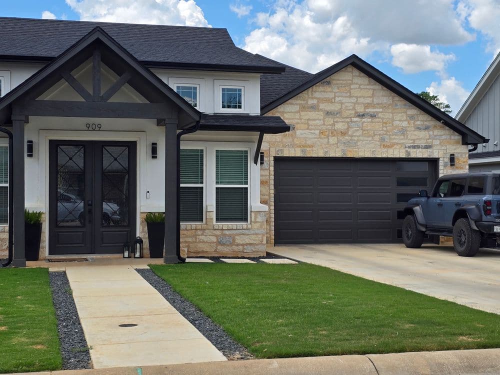 Modern house exterior featuring stone and dark trim, with a garage and SUV in driveway.