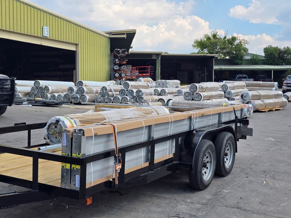 Rolls of material loaded on a trailer at a warehouse with stacks in the background.