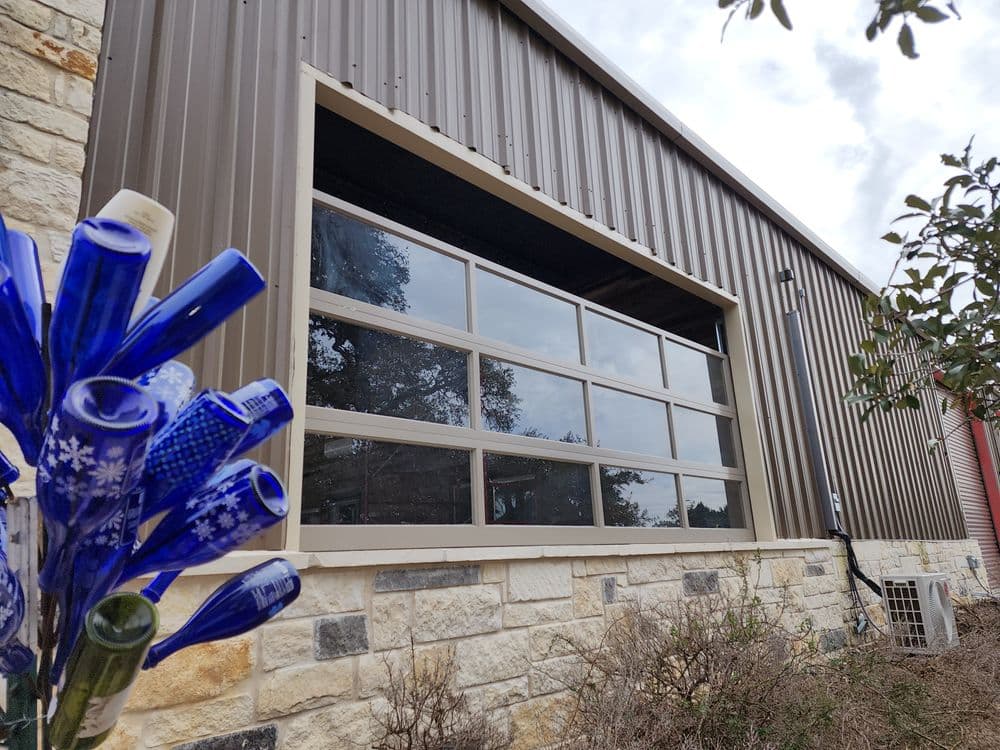 Modern industrial building with large glass windows and decorative blue bottle flowers in the foreground.