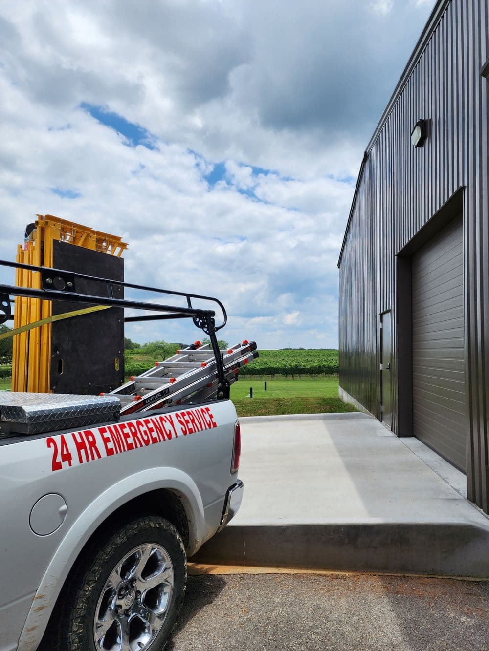 Emergency service truck parked outside a building with a loading area and green fields in background.
