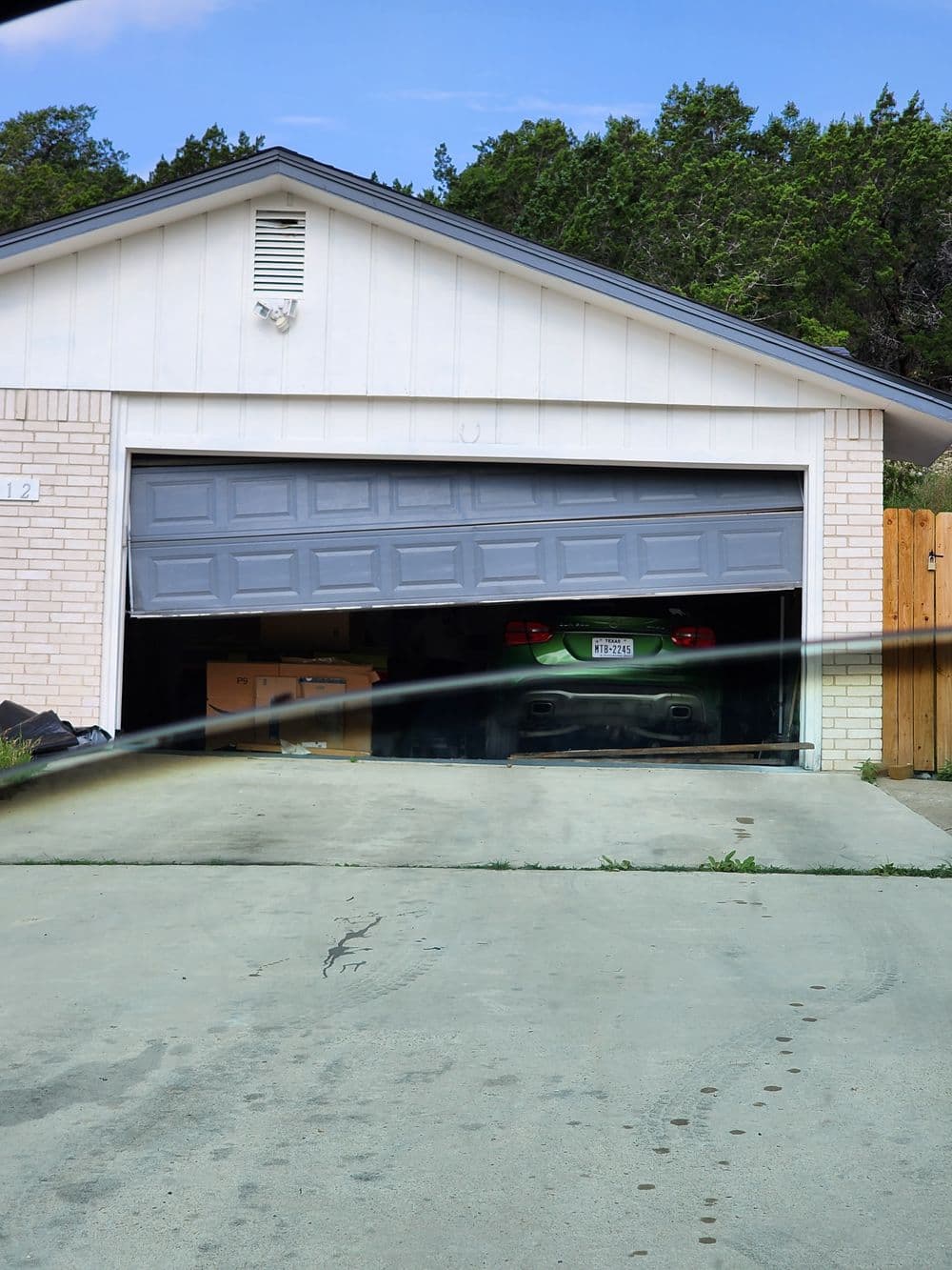 Green sports car partially visible in a garage with a gray door, residential setting.