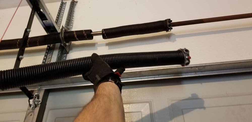 Hand replacing a garage door spring with safety gloves and tools in a home garage.
