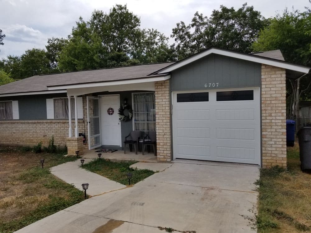 Single-story home with gray exterior, white garage doors, and a welcoming front porch.