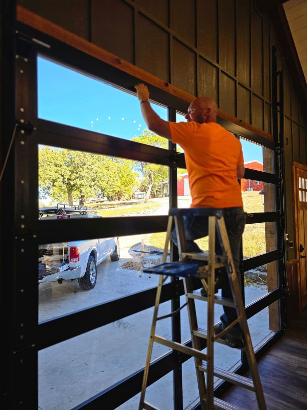Man in an orange shirt cleaning a garage door while standing on a ladder.