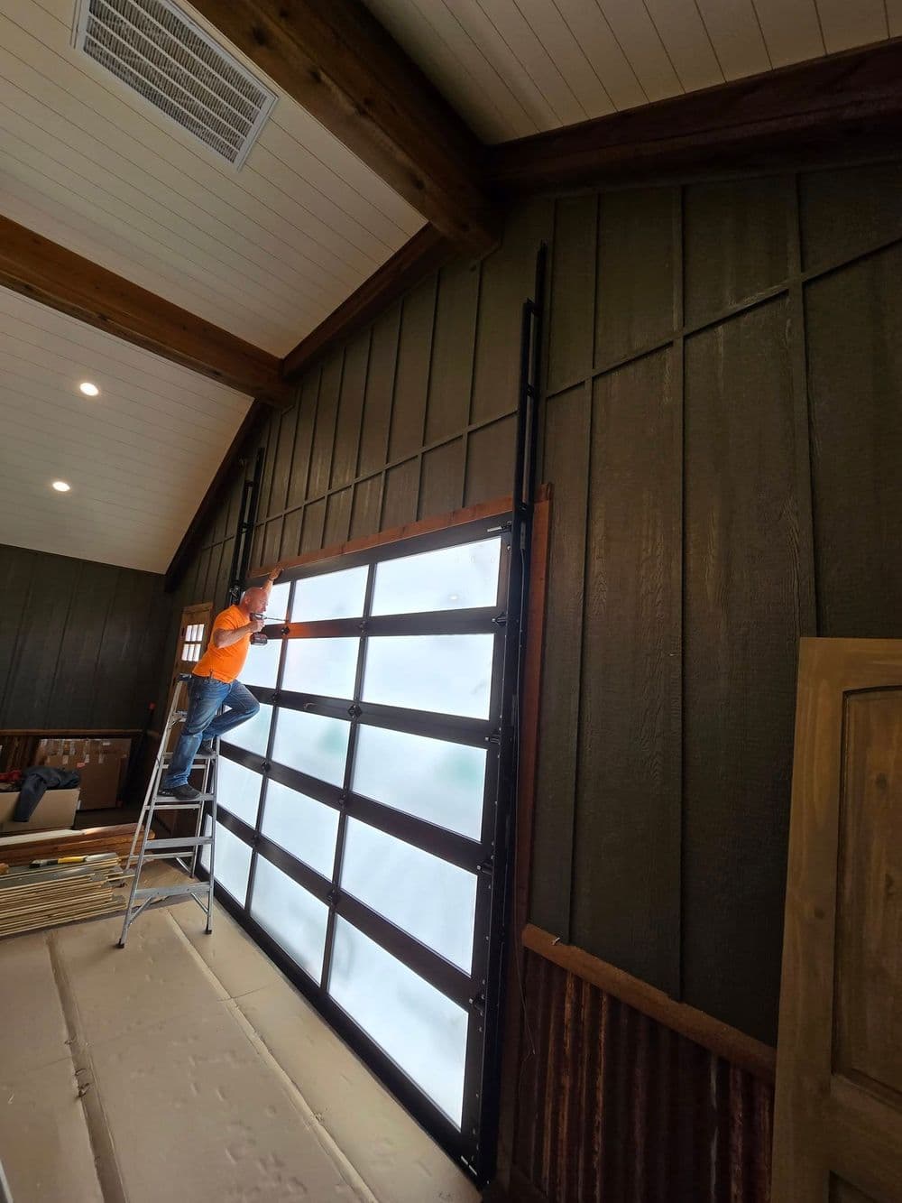 Person installing a glass garage door in a rustic interior setting with wooden beams.