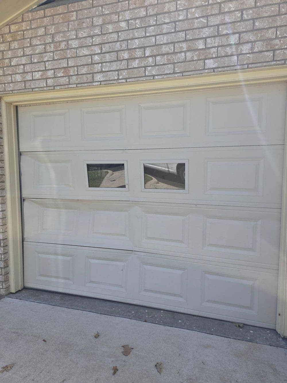 Damaged garage door with three panels and two small windows, showing signs of wear.