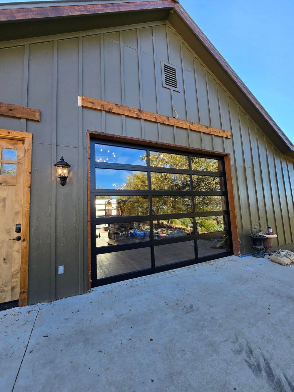 Modern glass garage door with black frames, wood accents, and a green metal exterior.