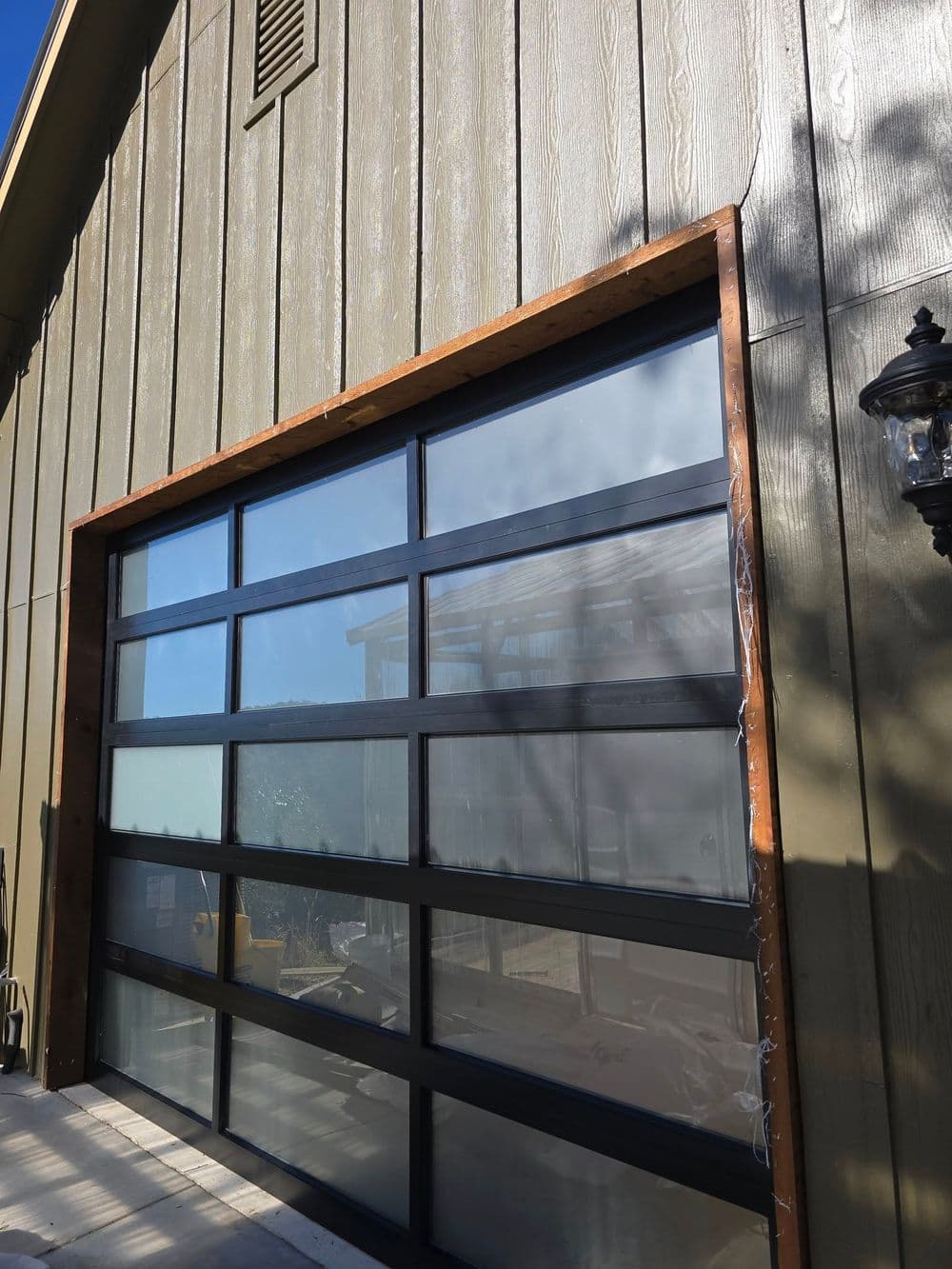 Modern glass garage door with black frame, set against a wooden building exterior.
